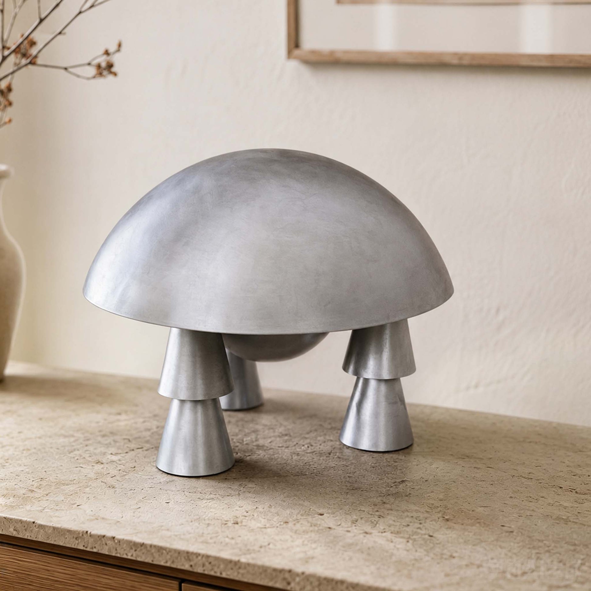 Silver space-age table lamp with a dome shade and conical legs on a stone console in a modern interior.